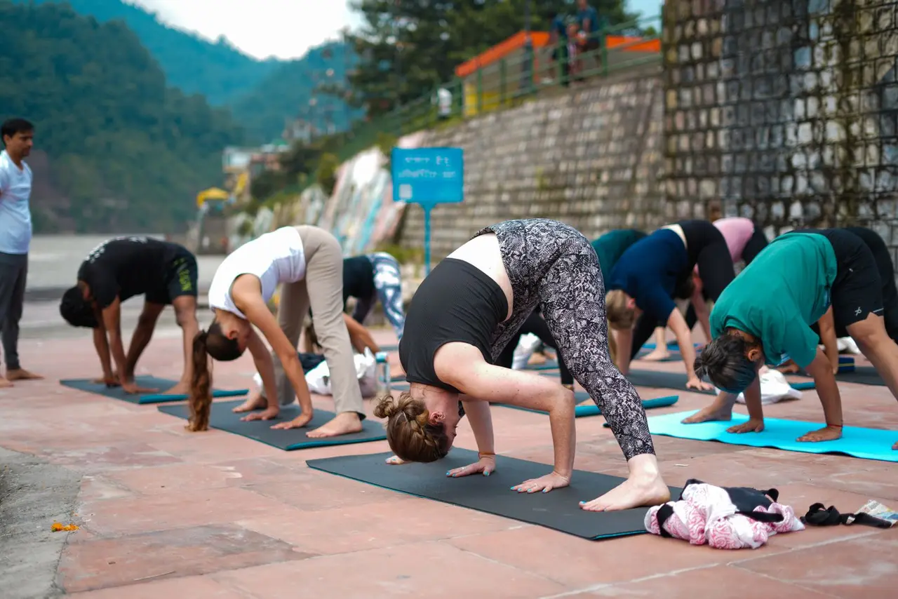 Group practicing yoga outdoors near river with scenic view, promoting wellness and mindfulness