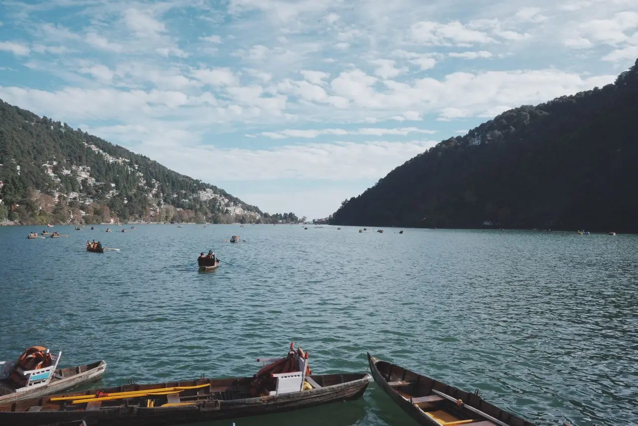 Picturesque view of boats on Nainital Lake surrounded by lush hills under a blue sky.